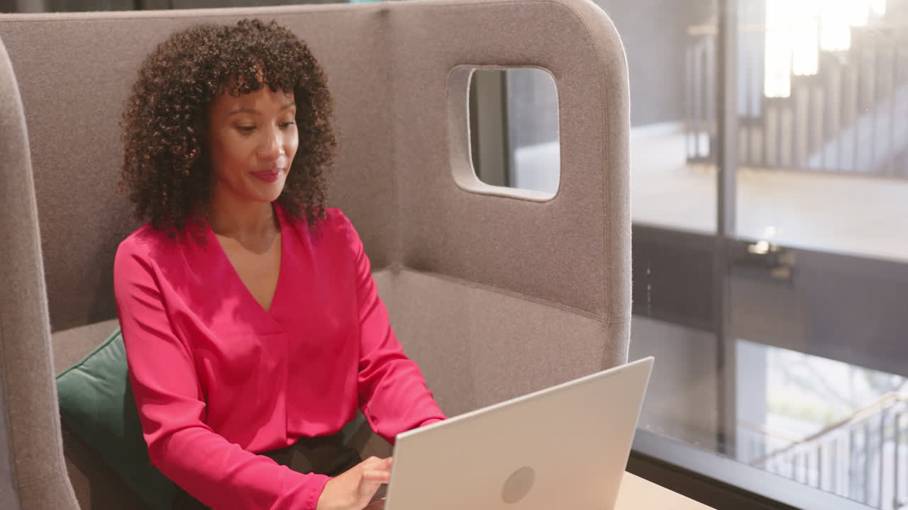 Using laptop, woman in pink blouse looking out window in modern office