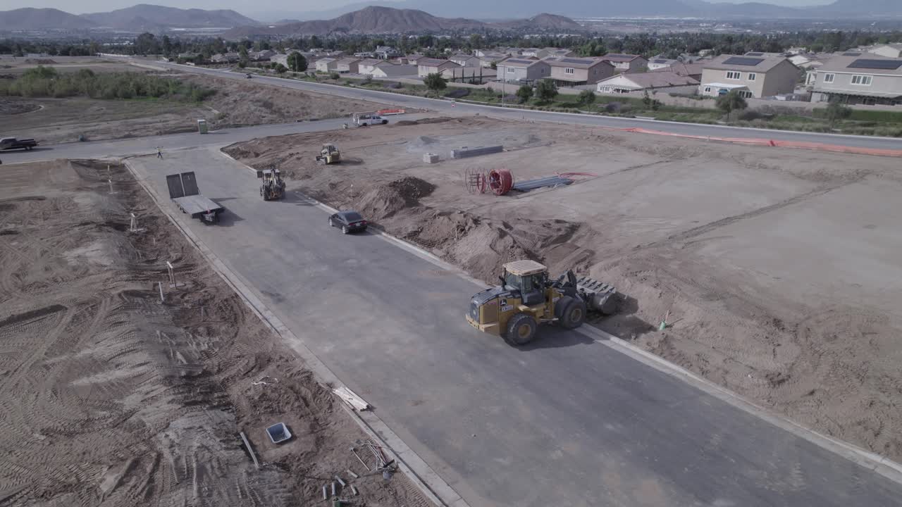 un avión no tripulado gira por encima de un cargador de ruedas en acción mientras mueve la tierra en un sitio de construcción, preparando el terreno para la futura construcción de viviendas
