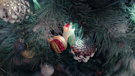 Cono-De-Pino-Esmerilado-Y-Adornos-Brillantes-Colgando-De-Agujas-De-árbol-De-Navidad---Primer-Plano,-Tiro-Inclinado-Hacia-Abajo