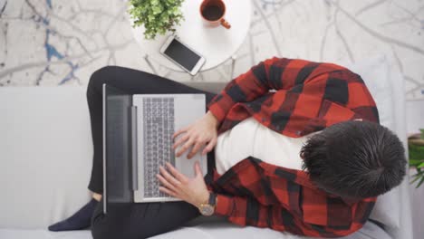 hombre joven sentado en el sofá en casa y mirando la computadora portátil.