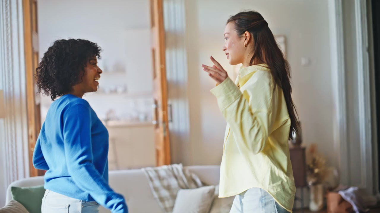 Female friends dancing together home. Playful women having fun indoors weekend.
