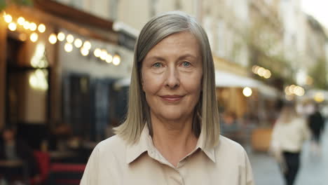 Close-Up-Of-Beautiful-Senior-Woman-With-Gray-Hair-Looking-Straight-At-Camera-And-Smiling-Cheerfully-At-City-Street