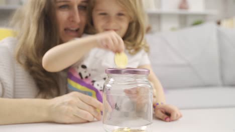 inversión en bitcoins. una niña con su madre pone bitcoins en la alcancía.
