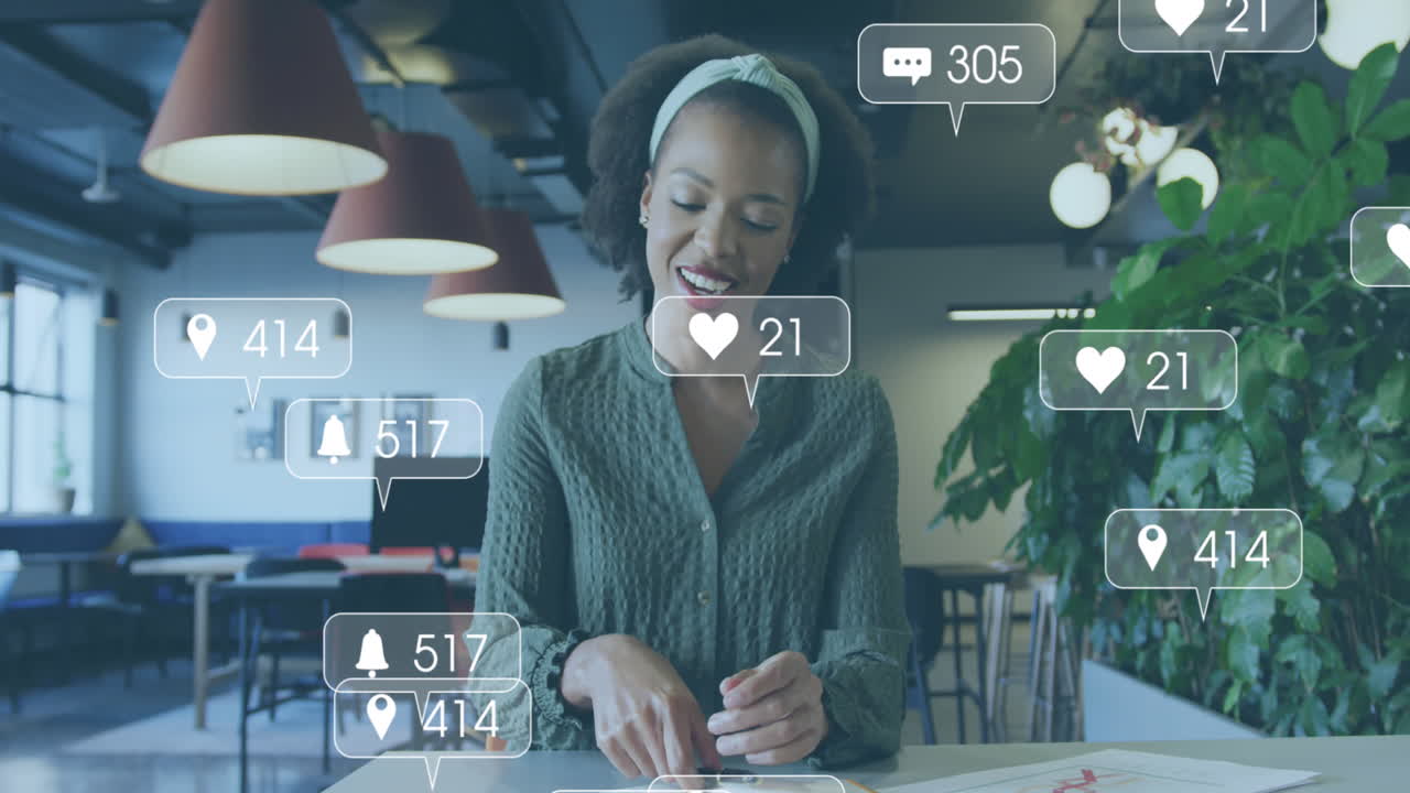 animación de iconos de redes sociales con números sobre una mujer de negocios afroamericana que trabaja en la oficina