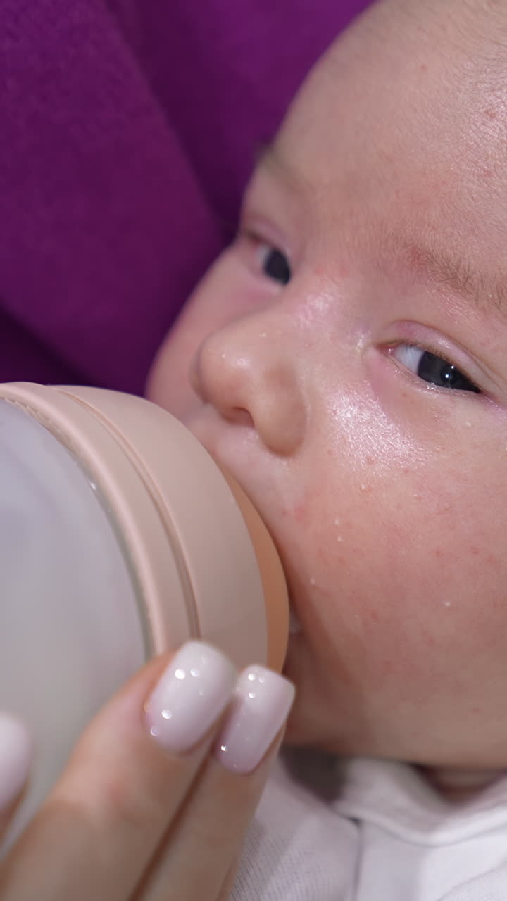 Baby being fed with milk from a bottle. Lovely child is suckling milk and moving his eyes right and left. Close up portrait. Vertical video