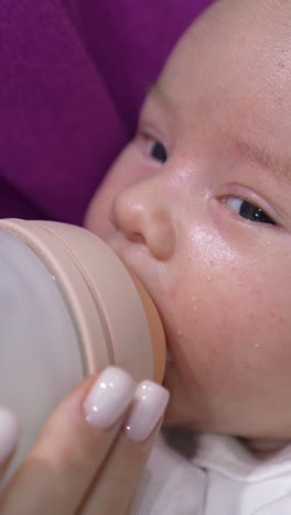 baby being fed with milk from a bottle. lovely child is suckling milk and moving his eyes right and left. close up portrait. vertical video