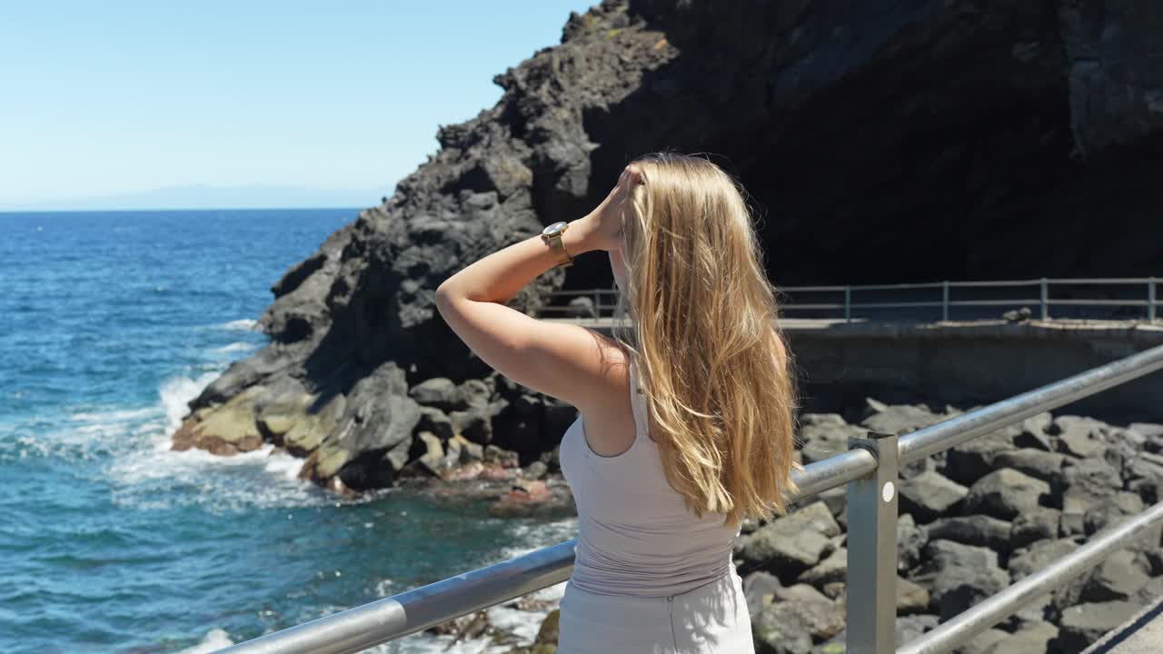 Beautiful blonde adjusting hair while admiring Tenerife island coastline