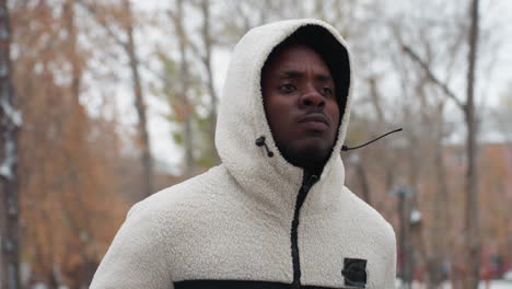 young adult in white hoodie jogging outdoors with blurred background of trees and buildings, showcasing active lifestyle and physical fitness in natural setting during daytime