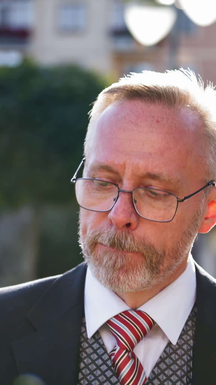 Thoughtful mature man smoke outdoors. Nervous middle aged businessman in glasses smoking cigarette standing on the city background. Vertical video