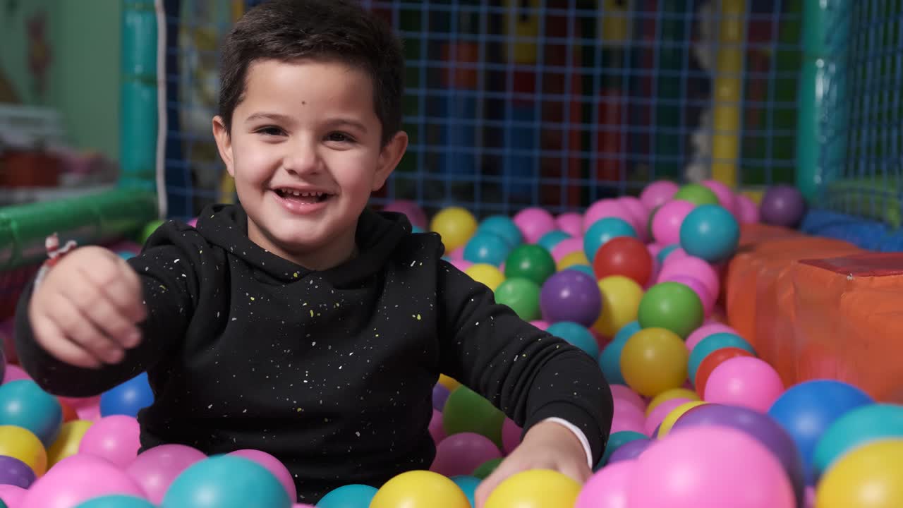 happy 5 year old boy with mask in a ball pool throwing balls to camera