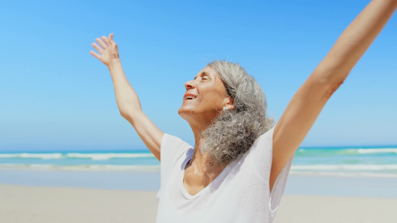 Front view of active senior African American woman with arms stretched out standing on beach 4k