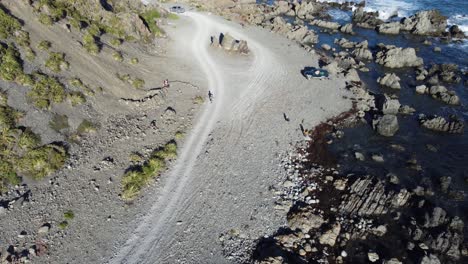 a high tilting shot of a motorcyclist driving along a gravel coastal road