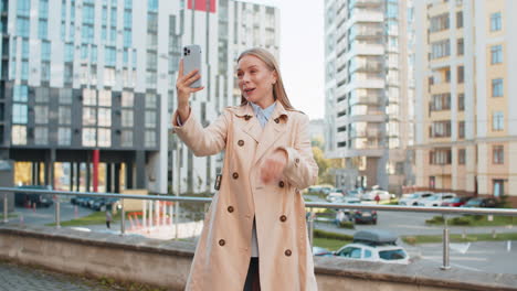 mature female blogger taking selfie on smartphone communicating video call online on downtown street