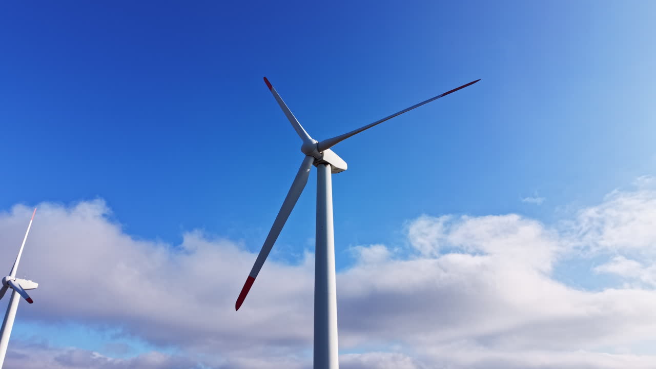 Le turbine eoliche si ergono maestose contro un cielo azzurro con nuvole, sfruttando l'energia del vento durante il giorno.