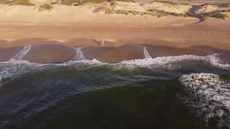 Man-walking-on-beach-during-sunrise,-aerial-side-view