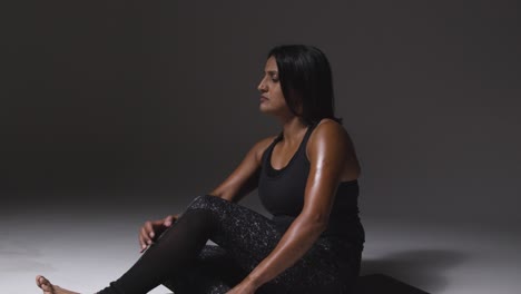 studio shot of mature woman wearing gym fitness clothing sitting on floor doing pilates stretching exercises