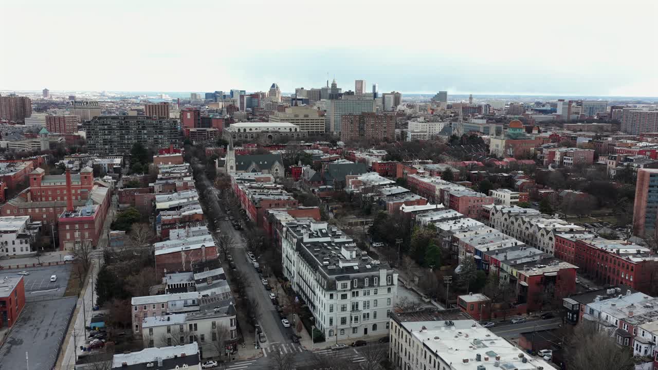 Luftfoto af Baltimore, Maryland, med en lang beboelsesgade kantet med rækkehuse, vintertagrygge, overskyet himmel og byens skyline i det fjerne. Sidebillede. Stille kvarter