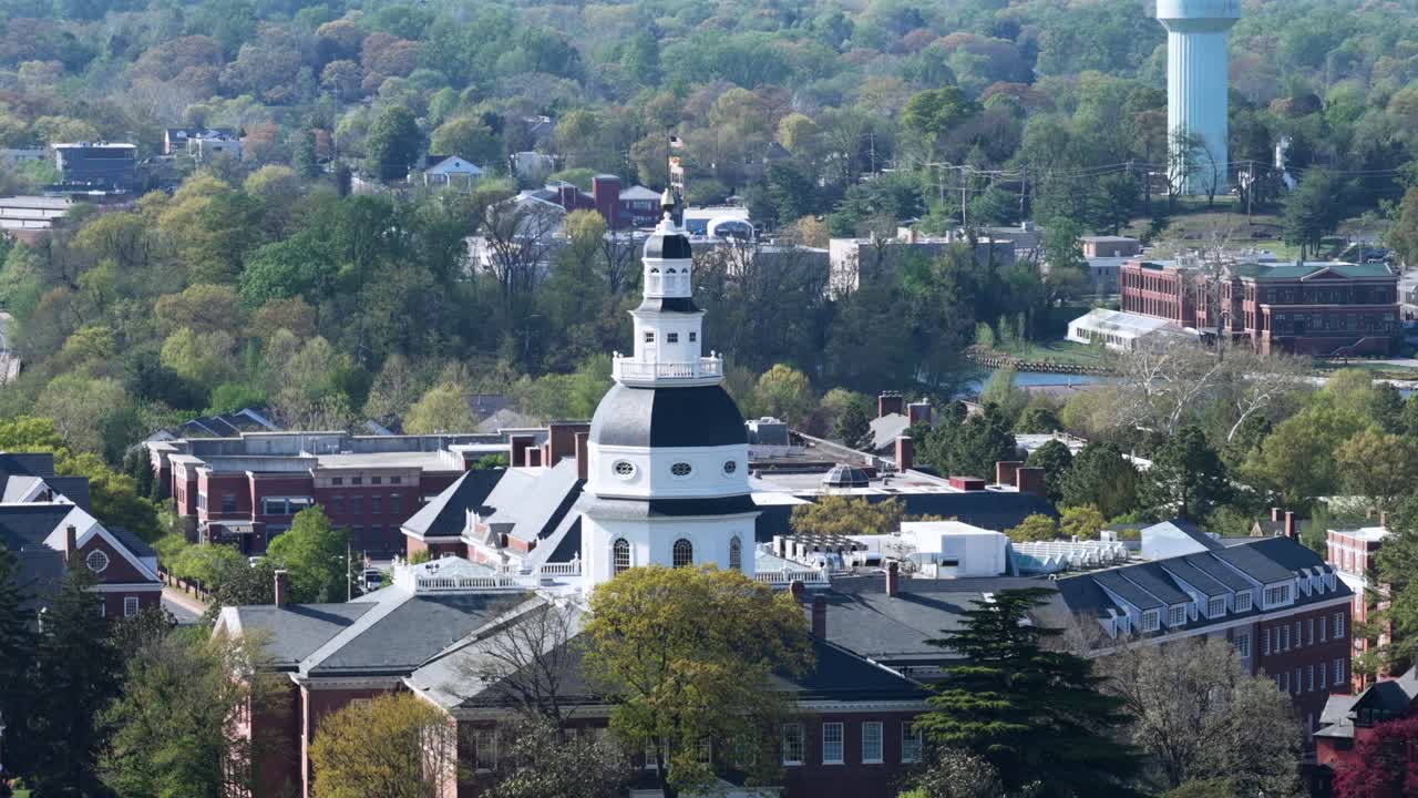 Toàn cảnh từ trên cao Nhà Quốc hội Maryland ở Annapolis, Hoa Kỳ, với kiến trúc mái vòm lịch sử được bao quanh bởi cây cối mùa xuân và các tòa nhà trung tâm thành phố dưới ánh sáng ban ngày dịu nhẹ trong khung cảnh thủ đô đẹp như tranh vẽ. Quay vòng quanh.