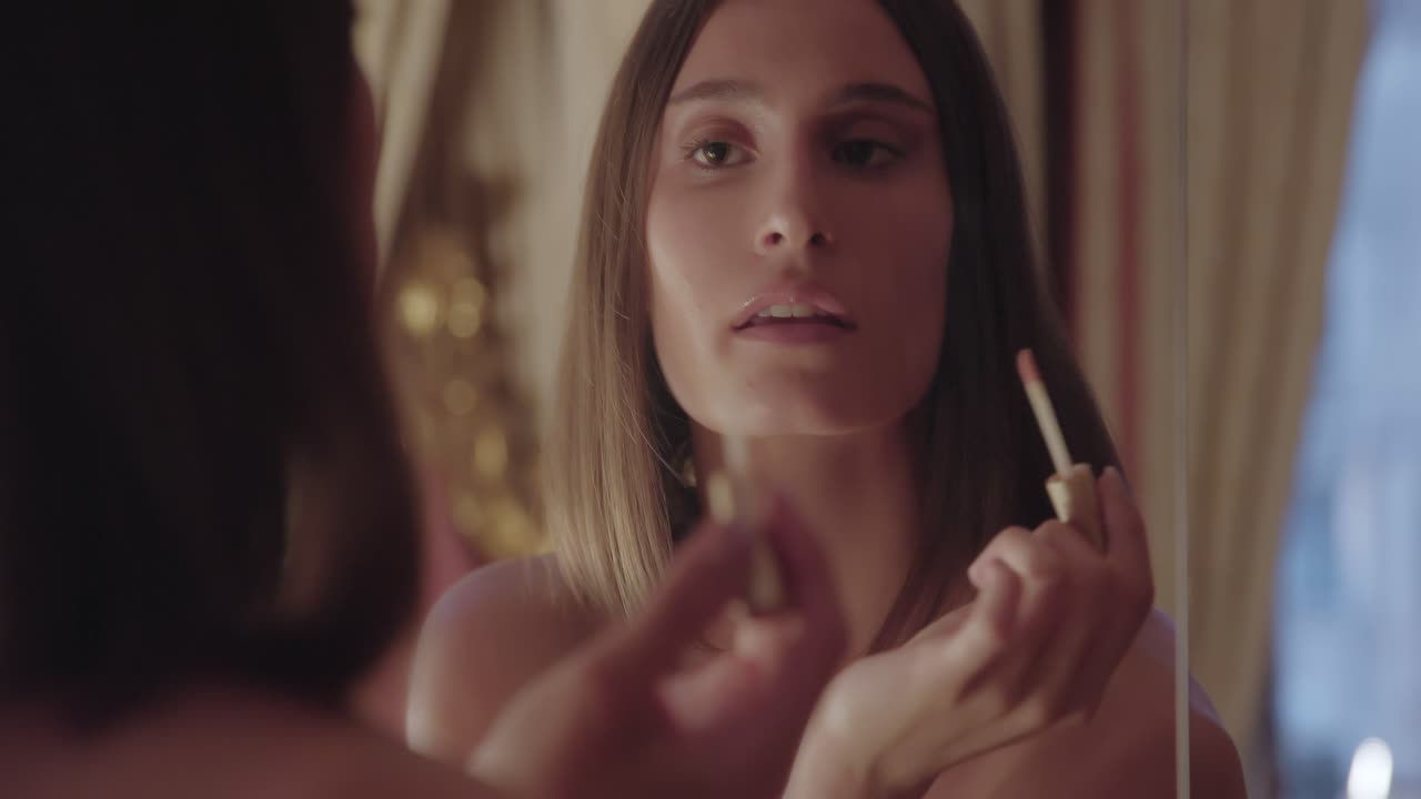 молодая женщина наносит блеск на губы возле зеркала