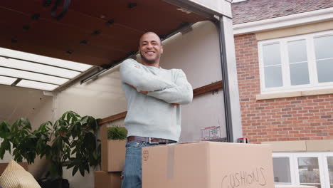 portrait of man unloading boxes from removal truck outside new home on moving day