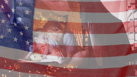 American-flag-waving-against-caucasian-mother-and-daughter-under-blanket-fort-at-home