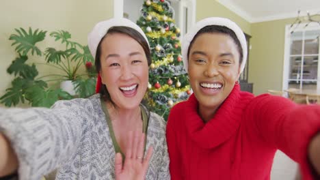 happy diverse female friends in santa hats making christmas video call, blowing kisses and smiling