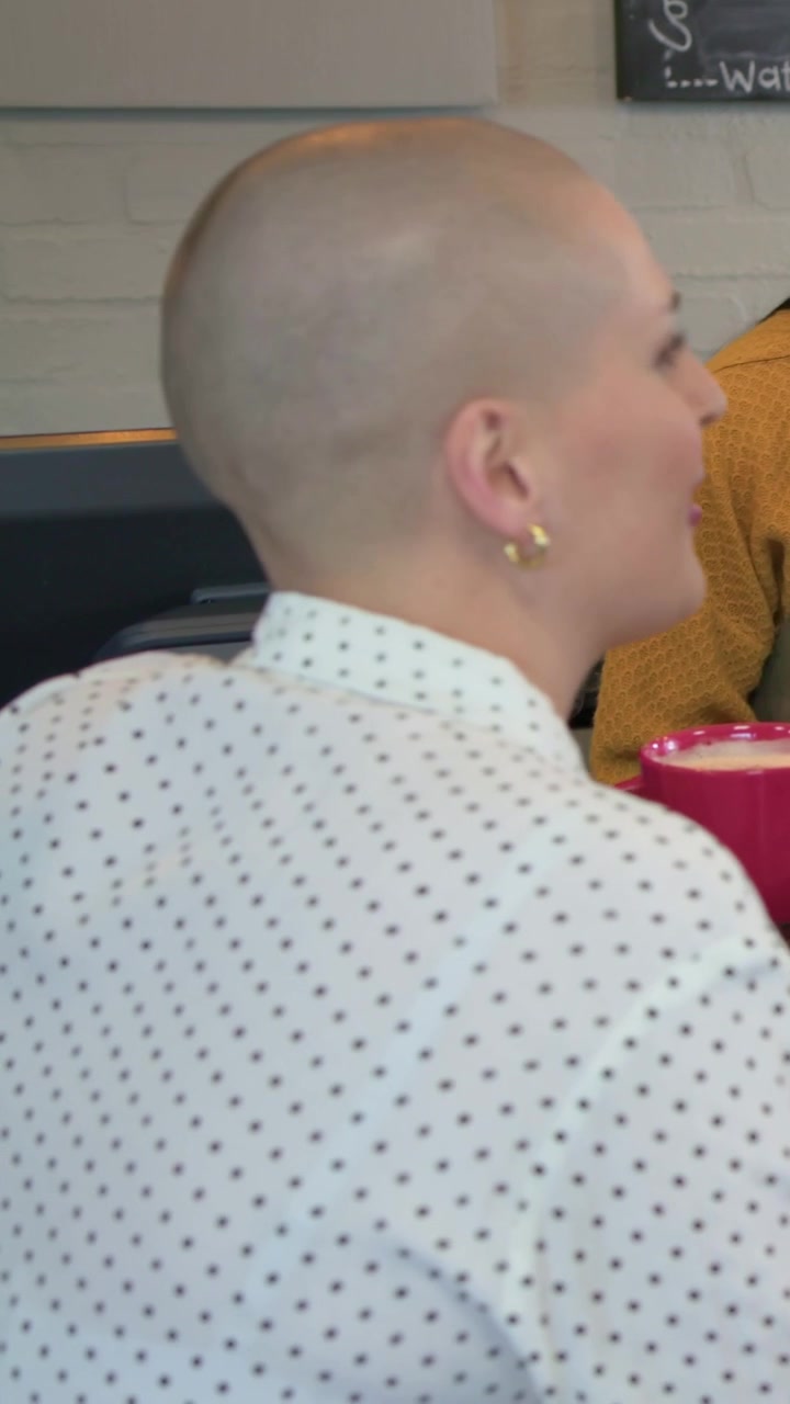 Video verticale: Cliente in ascolto con camicia a pois che si gira verso il personale che parla al bar, tazza rosa.