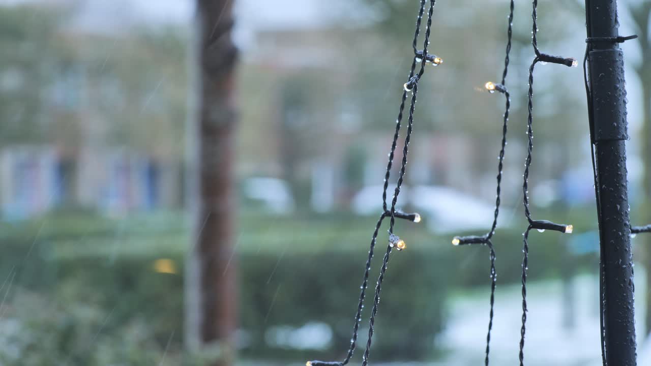 Close-up of sparkling fairy lights with water droplets against a blurred snowy neighborhood background during winter