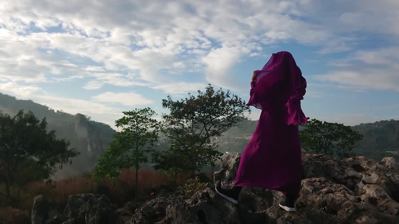 mujer islámica con burka púrpura se encuentra en una cumbre rocosa mirando el paisaje
