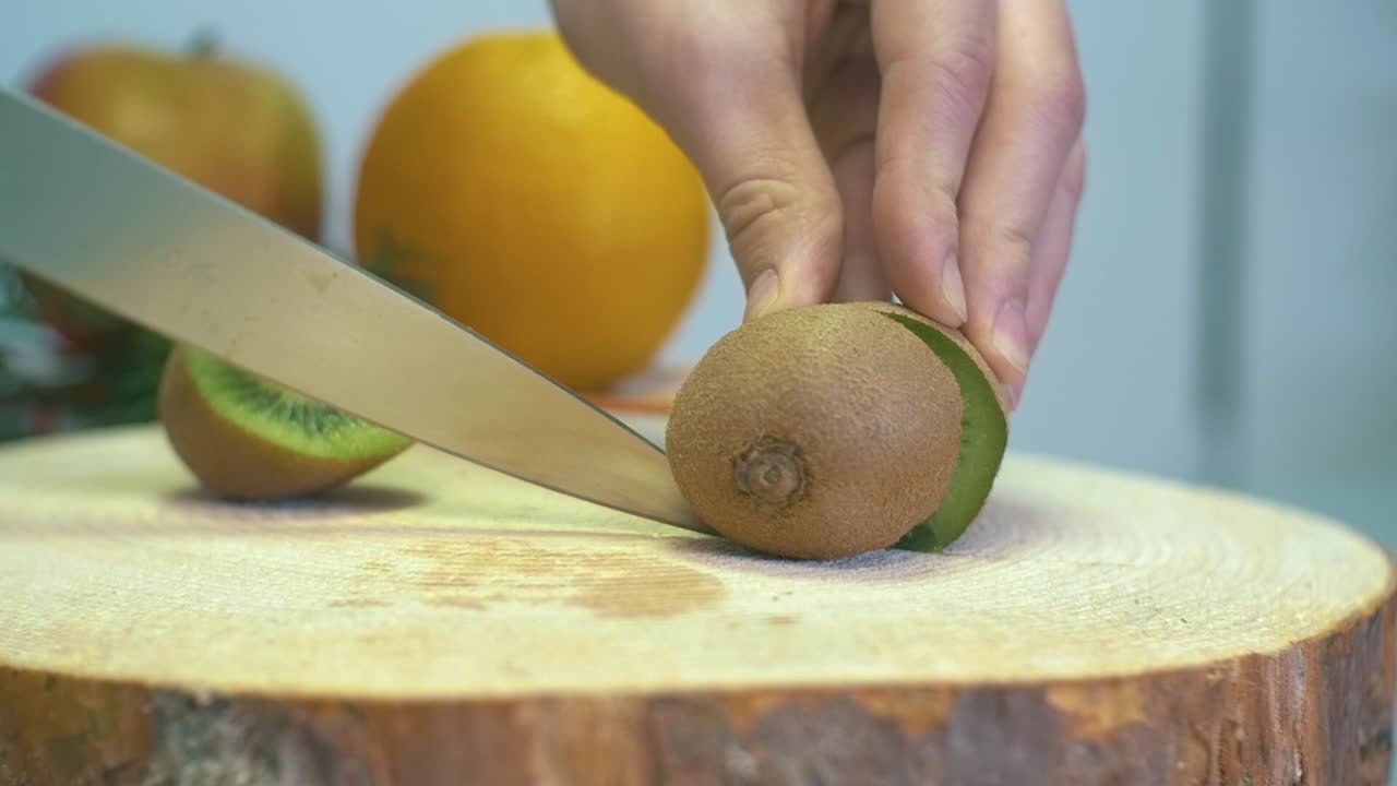 chica en cámara lenta cortando kiwi a mano con un cuchillo afilado cortando fruta de kiwi fresca de cerca en una tabla de cortar de madera