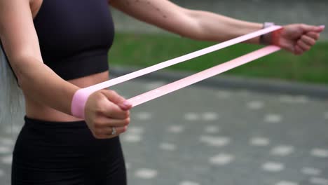 Unrecognizable-athletic-girl-engaged-in-fitness-wearing-black-sportswear-exercising-with-a-rubber-band-in-her-hands-in-a-summer