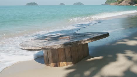 deserted beach in thailand with cable wheel in sand with waves lapping