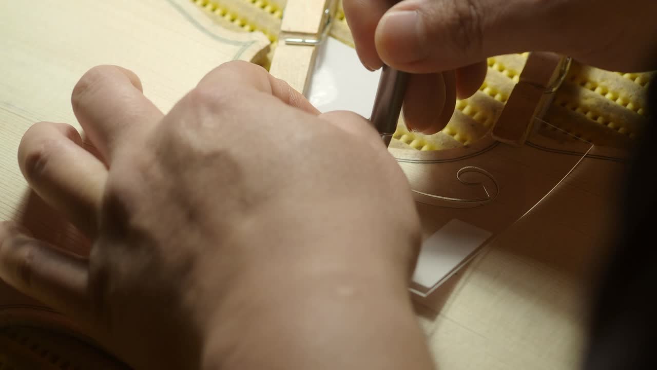 Luthier draws f-holes on violin top plate in a workshop, using specialized tools and tedchniques for a smooth, even finish that enhances resonance and aesthetics