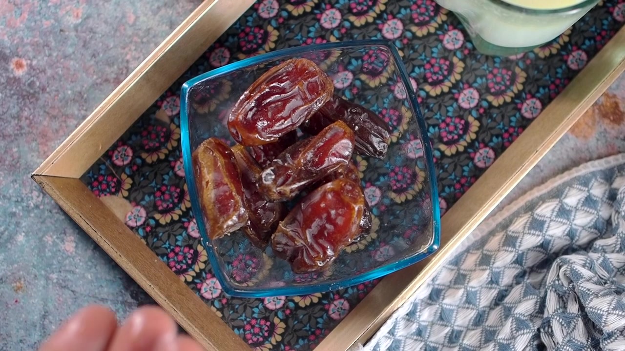 Hand Dropping Sweet Dried Dates into a Glass Bowl