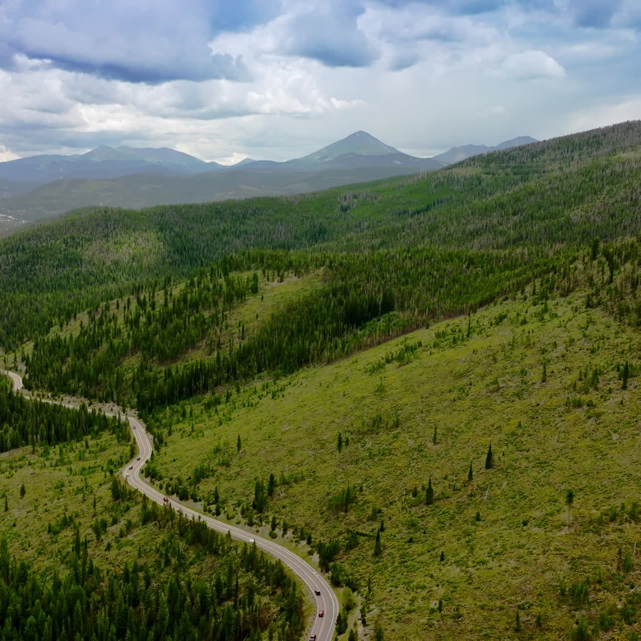Green mountainous territories covered with fir-trees and grass. Highway in the hills nearby the mountain river. Cloudy sky at backdrop