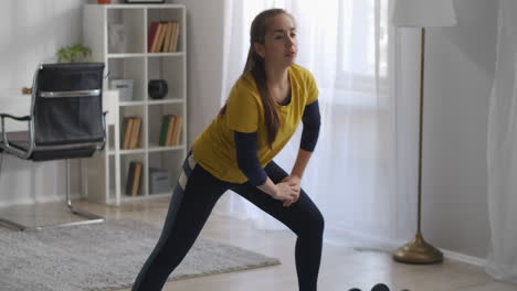 Agachada-En-La-Sala-De-Estar-Durante-El-Entrenamiento-Matutino,-Una-Adolescente-Está-Haciendo-Deporte-En-Casa-Durante-El-Autoaislamiento-En-Un-Estilo-De-Vida-Deportivo-Y-Saludable-Pandémico