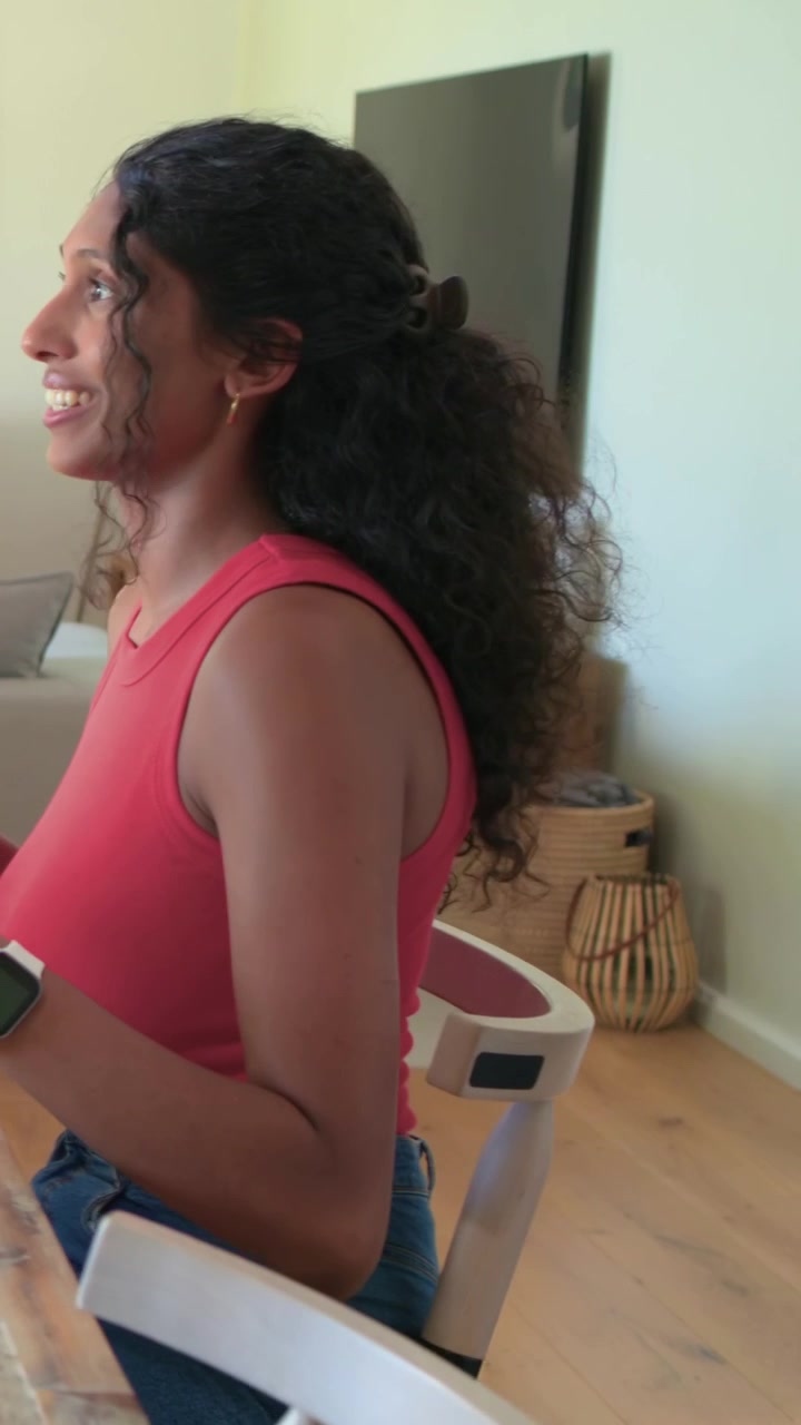 Video verticale: Donna con una maglietta rossa che reagisce all'allungo di un altro, allungandosi per prendere un piatto al tavolo di casa, con una forchetta.