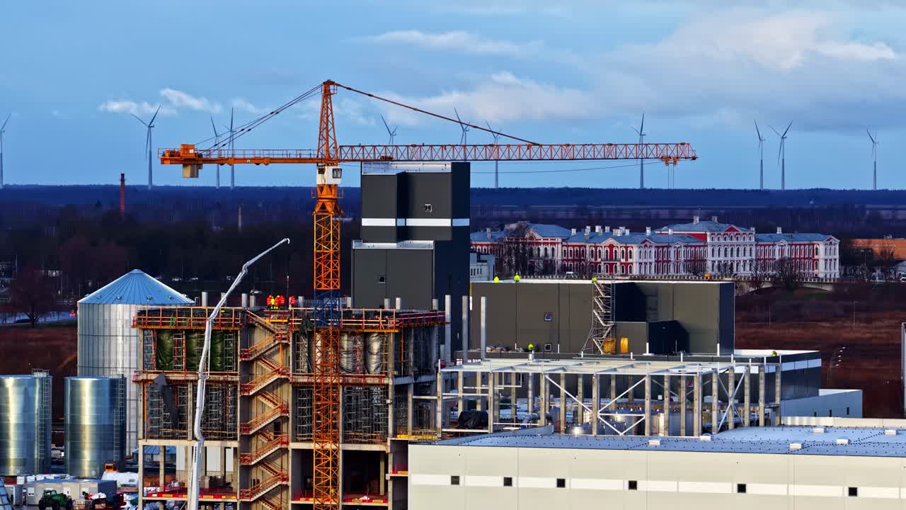 Construction Crane Towers Over Building Under Development At Industrial Site. ascending drone shot