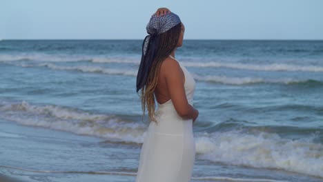 a female model at the beach looks on at the crashing waves