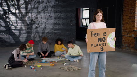 serious young environmental activist holding a cardboard with there is no planet b" inscription and looking at the camera"