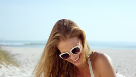 Woman-talking-selfie-using-phone-sitting-on-beach-wearing-designer-one-piece-swimsuit