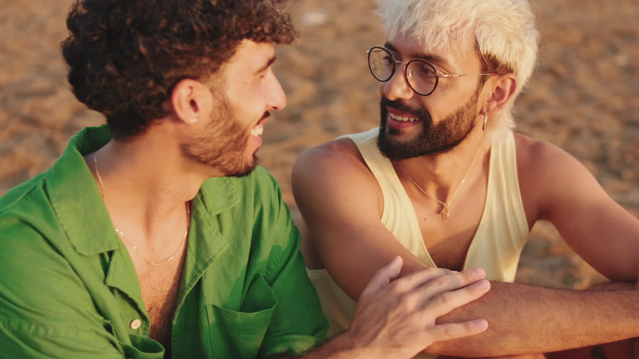 Due giovani uomini che parlano e sorridono su una spiaggia sabbiosa