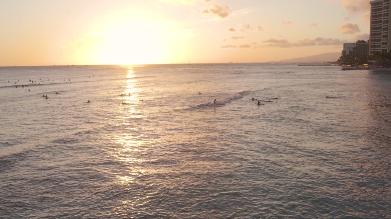 Surfers enjoy scenic golden hour sunset at Waikiki bay, Oahu island, Hawaii