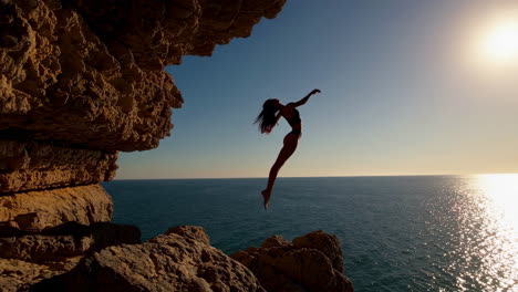 woman cliff jumping into the ocean at sunset