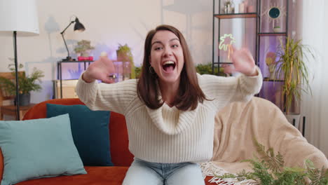 Pretty woman smiling friendly at camera waving hands gesturing hello hi greeting at home on sofa