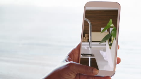 person holding smartphone with modern kitchen interiors displayed on screen