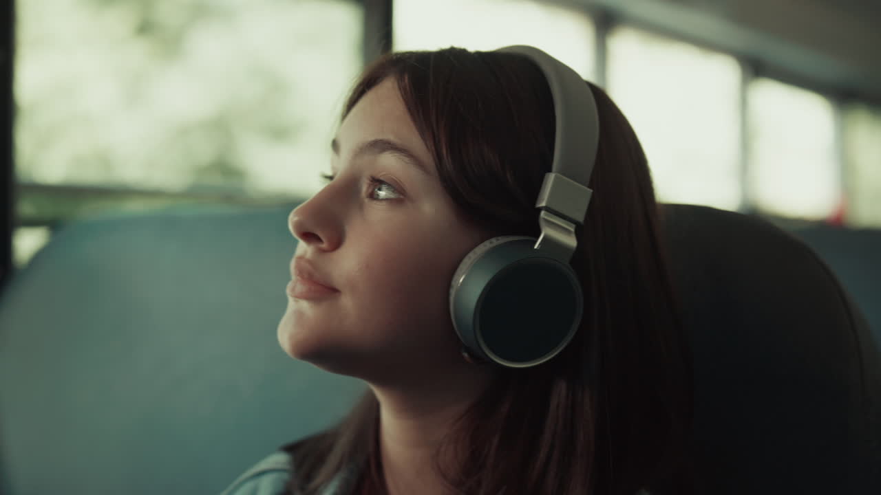 Nærbilde av en tenåringsjente som reiser med buss med hodetelefoner. Brunette som lytter til musikk.