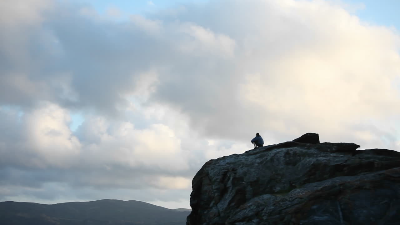 una persona se sienta en la cima de una montaña rocosa