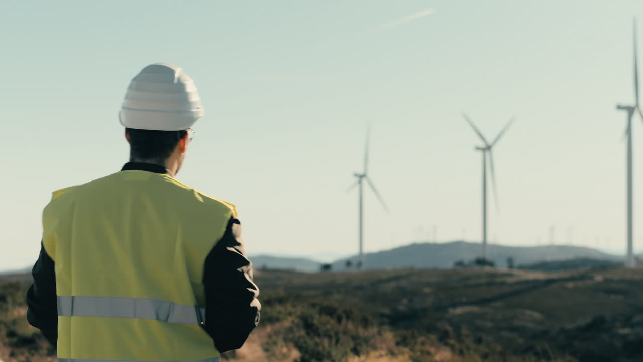 A white-helmeted engineer surveys wind turbines while walking, showcasing the technology behind renewable energy