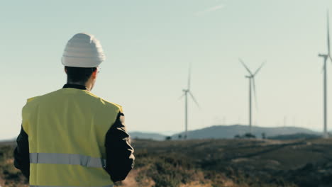 un ingeniero de casco blanco inspecciona las turbinas eólicas mientras camina, mostrando la tecnología detrás de la energía renovable